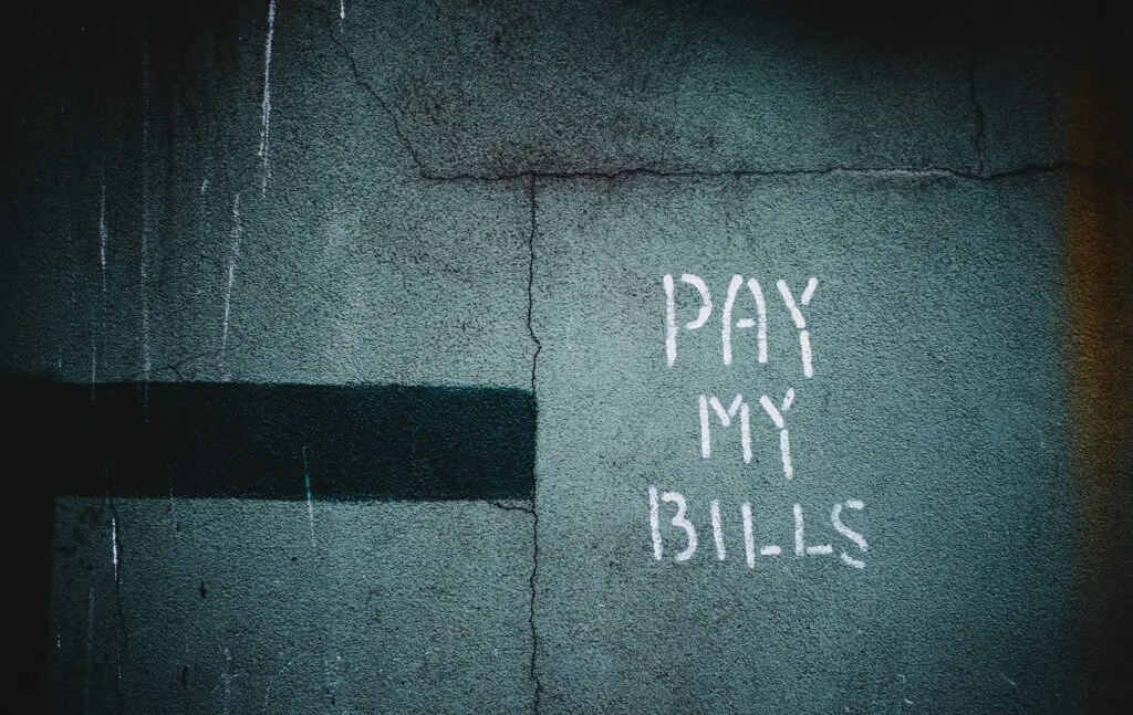 Handwritten “Pay My Bills” on a wall, symbolizing overdue invoices and illustrating How to Handle Late Payments for freelancers and small businesses.